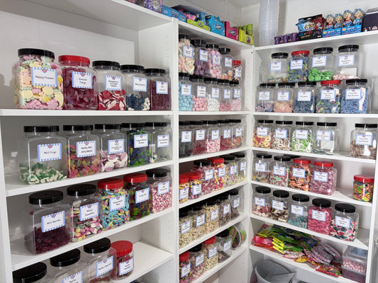 Shelves packed with clear plastic jars filled with various pick and mix sweets at Anderson's Sweet Shop in Swindon, including Haribo Mini Frogs, Dracula Fangs, and Happy Flowers.